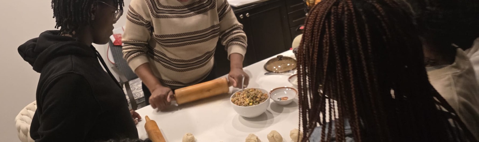 Mentor demonstrating dough rolling technique while youth watch